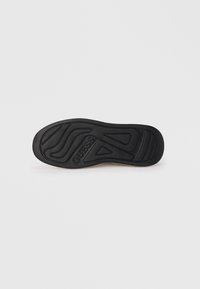 Semelle de sneaker en caoutchouc noir avec des motifs texturés et des accents surélevés, avec "GUESS" embossé sur le côté pour le marquage.