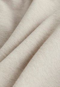 Světle béžová látka s texturovanou vazbou, vykazující jemné záhyby a hladký matný povrch. Žádné vzory ani akcenty nejsou viditelné.