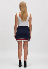 Marineblauer Strickrock mit taillierter Passform, der einen gestreiften Saum in Weiß, Rot und Blau hat. Kombiniert mit einem weißen Tanktop und schwarzen Schuhen.