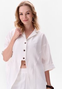 Witte kortekorte mouwen overhemd met een textuurstof, voorzien van vier donkere knopen en een cropped ontwerp dat het middel ontbloot.