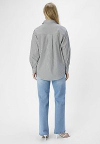 Gestreiftes Hemd in Schwarz und Weiß, lange Ärmel, lockere Passform, abgerundeter Saum. Kombiniert mit hellblauen Jeans und weißen Absatzsandalen.