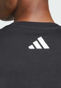 Sort bomulds t-shirt med et hvidt tre-stribe logo på den øverste ryg. Rund halsudskæring og ribbet tekstur.