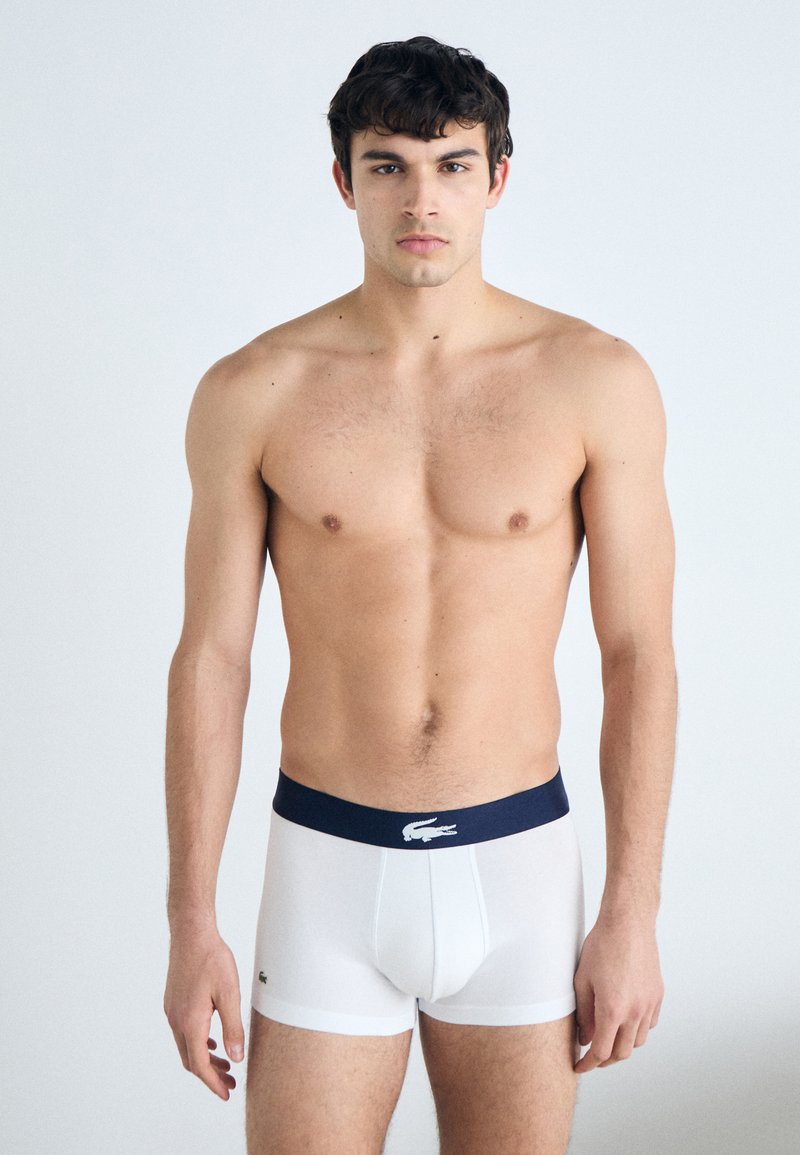 Men's white boxer briefs with a navy waistband featuring a logo. Made from smooth fabric, fitted design with short legs, front opening.