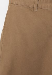 Tissu en coton marron avec une texture lisse. Vue en gros plan mettant en valeur les coutures et les assemblages, illustrant un design classique.