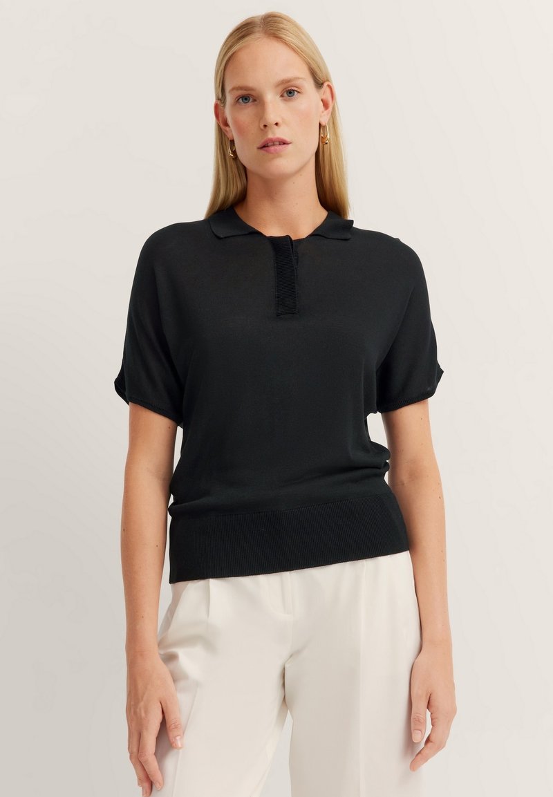 Schwarzes Poloshirt mit kurzen Ärmeln, geripptem Kragen und Saum, ausgestattet mit einer Knopfleiste. Glatte Textur, entworfen für eine körpernahe Silhouette.