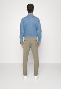 Camicia di jeans con chiusura a bottoni, maniche lunghe e colore blu chiaro, abbinata a pantaloni khaki a gamba affusolata e sneakers bianche.