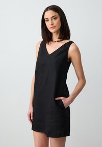 Schwarzes Leinen-Ärmelloses Kleid mit V-Ausschnitt, Seitentaschen und einem lockeren Sitz, das eine glatte, leicht strukturierte Oberfläche aufweist.