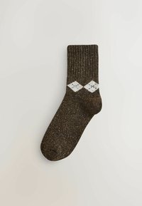 Brun, texturerad socka med ribbad kant, glittrigt material och ett vitt diamantmönster med små svarta detaljer.
