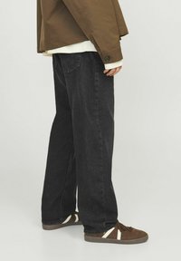 Mustad denim teksad, lahtise lõikega, nähtava õmblusega ja kahe tagataskuga, koos pruuni jope ja pruuni tossudega.