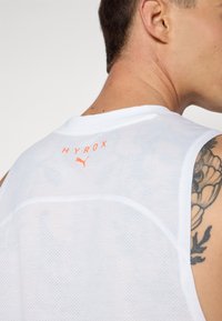 White, sleeveless athletic tank top featuring a mesh texture. "HYROX" logo in orange on the upper back, with minimal stitch detailing.