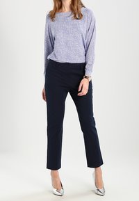 Blusa de manga larga azul y blanca con un estampado, combinada con pantalones ajustados color navy y tacones altos plateados. Tejidos suaves; la blusa tiene un corte relajado.