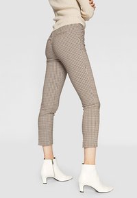 Kostkované kalhoty v béžové a hnědé barvě, úzký střih s krátkou délkou. Kombinovány s bílými kotníkovými botami se zipy na straně.