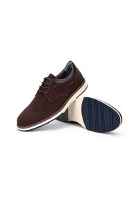 Chaussures oxford en daim marron avec des accents en cuir noir et une semelle blanche, dotées d'une semelle extérieure en caoutchouc bleu texturé et d'un bout arrondi.