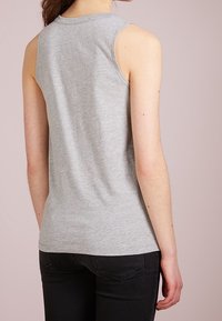 Haut sans manches gris en tissu doux, avec un col rond et une coupe ajustée. Le dos présente une texture lisse et non ornée.
