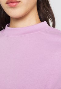 Felpa di colore viola chiaro con scollo a girocollo a costine. Tessuto morbido, con superficie liscia e dettagli di cuciture sottili.