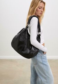 Grande borsa a spalla in pelle nera con una texture morbida, forma curvata e una tracolla resistente con dettagli in metallo.