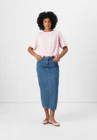 Rosa teksturert topp med korte ermer og en liten logo, kombinert med et høyt liv denim maxiskjørt. Beige flate sko fullfører antrekket.