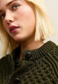 Gebreide groene cardigan met een geribbelde kraag en twee donkere knopen, met een gemarmerd patroon en een kort gesneden stijl.