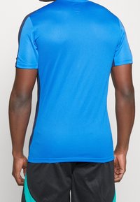 Kortärmad träningsskorta i klarblått tyg med texturerad yta, med mörkblå accenter längs sidsömmarna och axlarna.