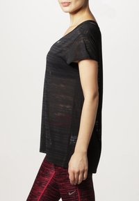 Camiseta negra de corte holgado con sutiles rayas horizontales, mangas cortas y escote amplio, combinada con leggings rojos con estampado.