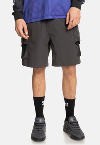 Korte cargobroek van donkergrijze stof, met grote zijzakken, een relaxte pasvorm en een vlakke zoom. Gecombineerd met zwarte sportieve sokken en schoenen.