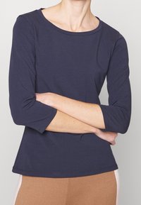 Top fitted in blu scuro, con maniche lunghe e scollatura rotonda, realizzato in un tessuto morbido. Design semplice senza pattern o dettagli visibili.