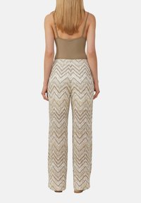 Bodysuit beige avec bretelles réglables associé à un pantalon ample à motif chevron dans des tons crème et châtaigne, présentant un tissu texturé.
