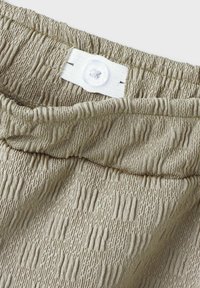 Beige gestructureerde stof met een gathered elastische tailleband en knoopsluiting. Gladde oppervlakte met verticale streepprint.