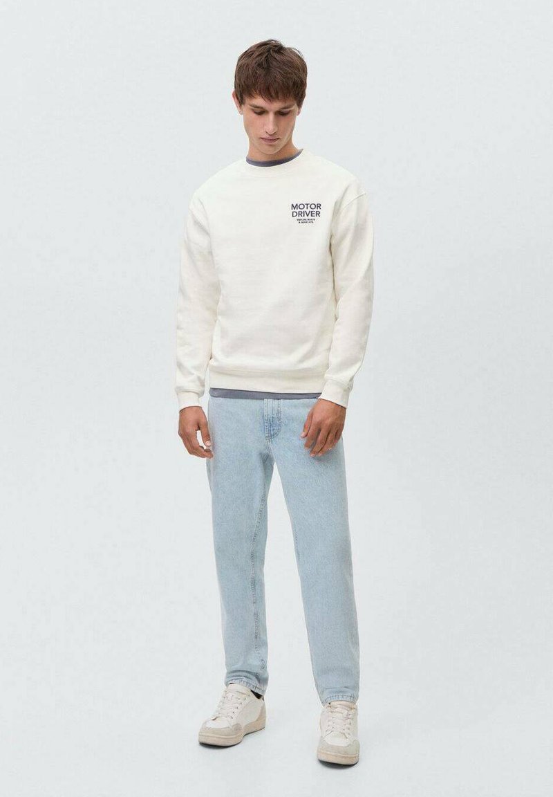 Felpa color crema con scollatura rotonda e testo stampato sul petto, abbinata a jeans azzurri chiari e sneakers bianche.