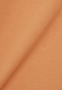 Tejido de punto suave de color marrón claro con una textura lisa, mostrado en un primer plano que resalta las costuras finas y pliegues suaves.