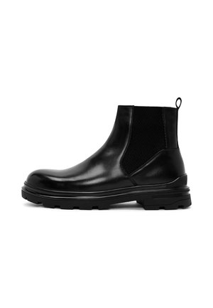 Botte Chelsea en cuir noir avec panneau latéral élastique, languette à l'arrière, et semelle épaisse en caoutchouc avec crampons pour l’adhérence.