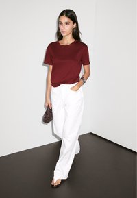 Maroon short-sleeve t-shirt paired with white wide-leg trousers. The outfit includes a dark woven handbag and black flip-flops. Simple design.