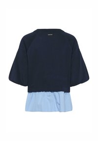 Granatowa kurtka crop top z bufkami na rękawach, nałożona na jasnoniebieską koszulę w drobne prążki z falbanką na dole.
