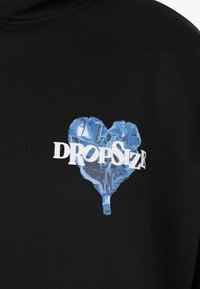 Blue foil heart balloon with white "DROPSIZE" text across it printed on black fabric.