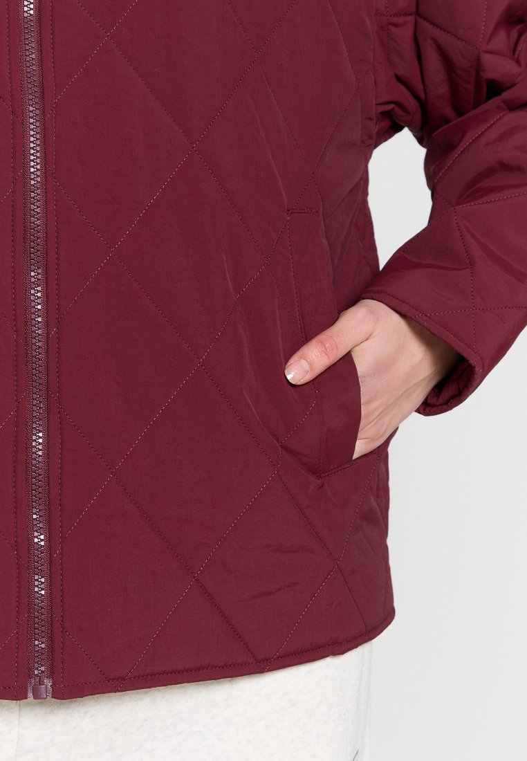 Chaqueta acolchada burdeos con patrón de diamante, que cuenta con cremallera frontal y bolsillos laterales, fabricada en un tejido ligero y suave.