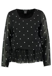 Blusa nera a maniche lunghe con pois bianchi, scollatura tonda e orlo plissettato. Realizzata in tessuto leggero e trasparente.