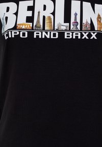 Schwarzes T-Shirt mit dem Wort "BERLIN" in großen Buchstaben, mit Bildern von ikonischen Wahrzeichen darüber und "CIPO AND BAXX" darunter in fetter weißer Schrift.
