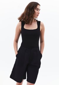 Zwarte mouwloze bodysuit met een vierkante hals, gecombineerd met zwarte op maat gemaakte shorts met zijzakken en een losse pasvorm.