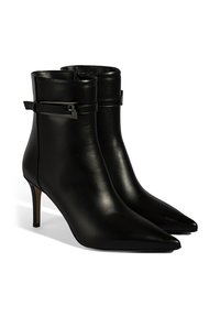 Bottes courtes en cuir noir avec un bout pointu, un talon fin et une bride latérale ornée d'un accent métallique. Texture lisse et design ajusté.