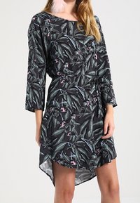 Vestido negro con un patrón de hojas botánicas en verde y rosa. Mangas largas, corte relajado y un dobladillo asimétrico. Tejido ligero.