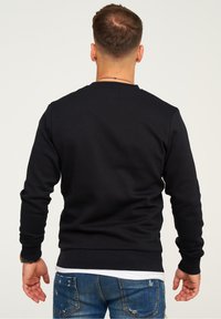 Black sweatshirt with long sleeves and round neck, featuring ribbed cuffs and hem, worn over a white shirt, with a plain design.