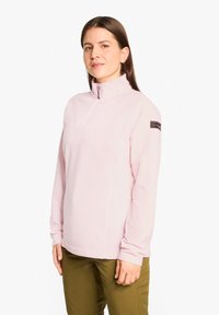 Helles rosa Fleece-Pullover mit hohem Kragen und halbem Reißverschluss. Mit langen Ärmeln und einem Logo-Patch auf der linken Schulter.