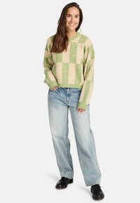 Beige en groene geblokte gebreide trui, ontspannen pasvorm, geribbelde manchetten, gedragen met lichte baggy jeans en zwarte schoenen. Getextureerd stofdetail.