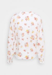 Blouse blanche à manches longues avec un motif floral en nuances de rose et de jaune, agrémentée de petits points. Le dos présente un col simple et des poignets boutonnés.