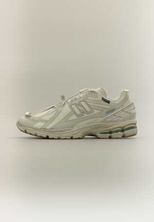 Lyse beige New Balance 1906R løbesko med mesh-overdel, synlig polstring i sålen og "GORE-TEX" mærkat på siden.