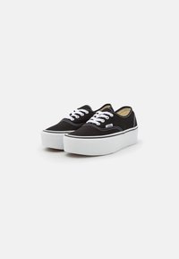 Black canvas sneakers with white laces, white rubber sole, and contrasting stitching. Features a low-top design and rounded toe.
