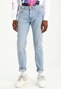 Ljusblå jeans med rak passform, hög midja, fem fickor och uppvikta nederkanter. Kombinerat med vita sneakers.