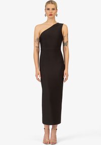 Zwarte midi-jurk met één schouder, een getailleerde silhouette, gladde stof en een rechte zoom. Geaccentueerd met minimalistische lichtbruine hoge hakken.