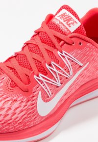 Gros plan d'une chaussure de course rouge Nike Zoom Winflo 5 avec logo Swoosh blanc et lacets détaillés sur un fond clair.