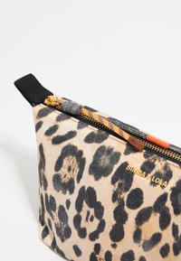 Kozmetická taška s leopardím vzorom v béžovej a čiernej textílii. Obsahuje zlatý zips s textúrovaným úchytom a logo v zlatom písmene na boku.